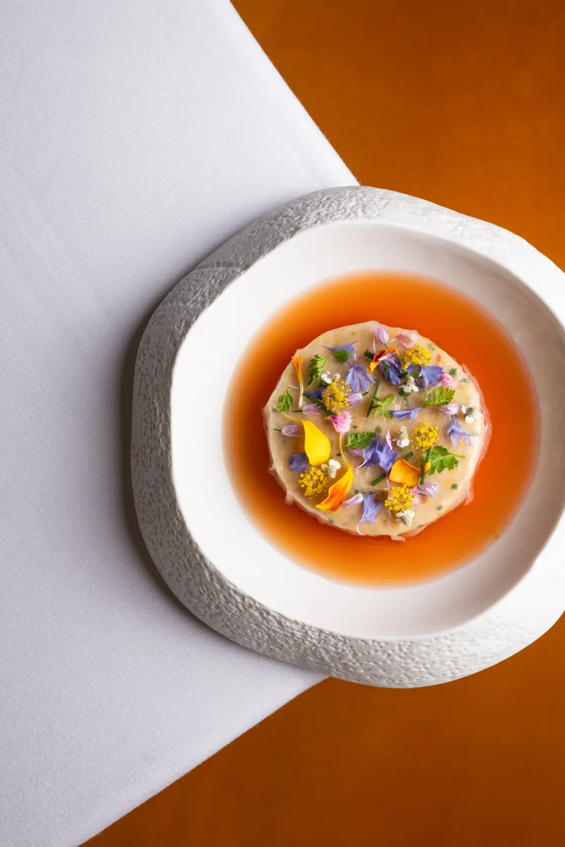 Consommé gastronomique paré de fleurs comestibles, vue de dessus sur nappe blanche