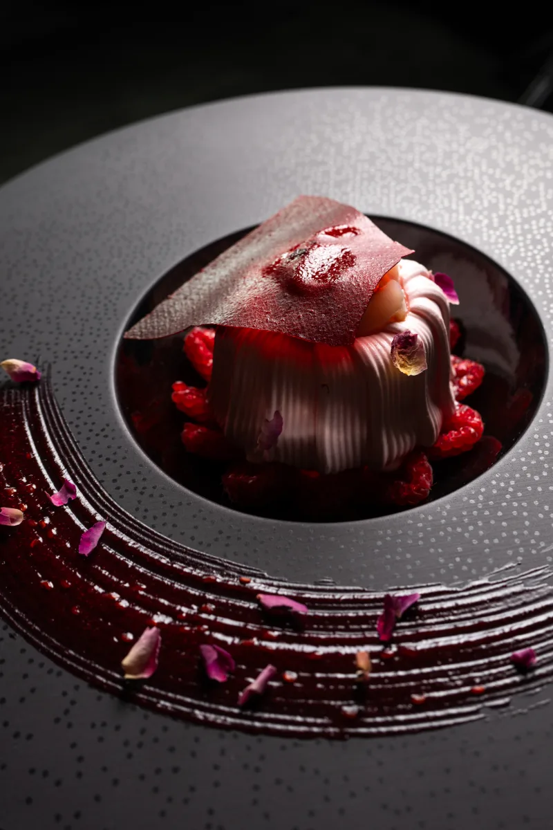 Dessert aux framboises et pétales de rose, trait de coulis sur assiette anthracite