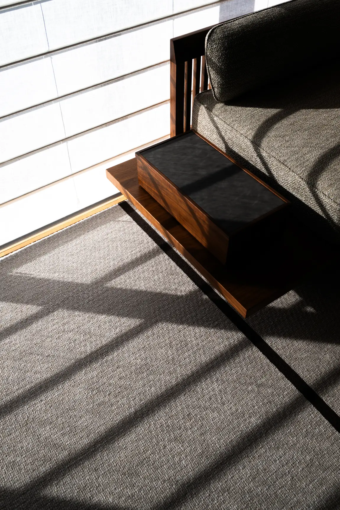 Fauteuil en bois et bouclé baigné d'une lumière rasante sur tapis texturé